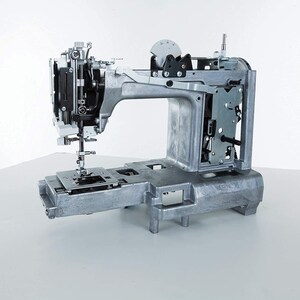 May include: A silver sewing machine with the front panel removed, revealing the internal workings. The machine is on a white surface.