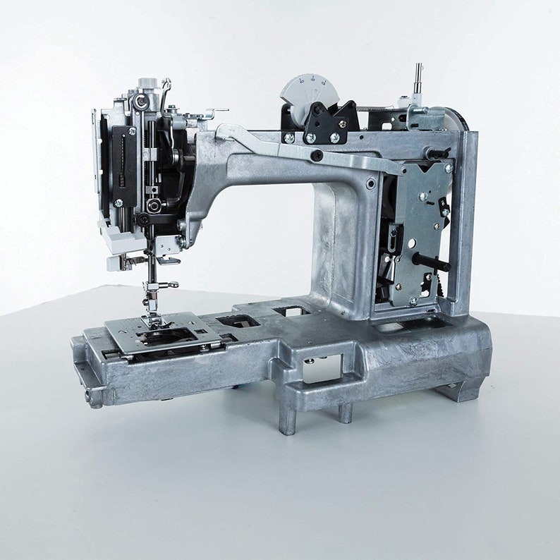 May include: A silver sewing machine with the front panel removed, revealing the internal workings. The machine is on a white surface.