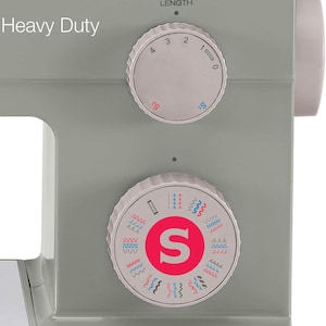 May include: A gray sewing machine with a white label that reads "Heavy Duty". The machine has two dials, one for stitch length and one for stitch selection. The stitch selection dial has a red "S" in the center and shows a variety of stitch patterns.
