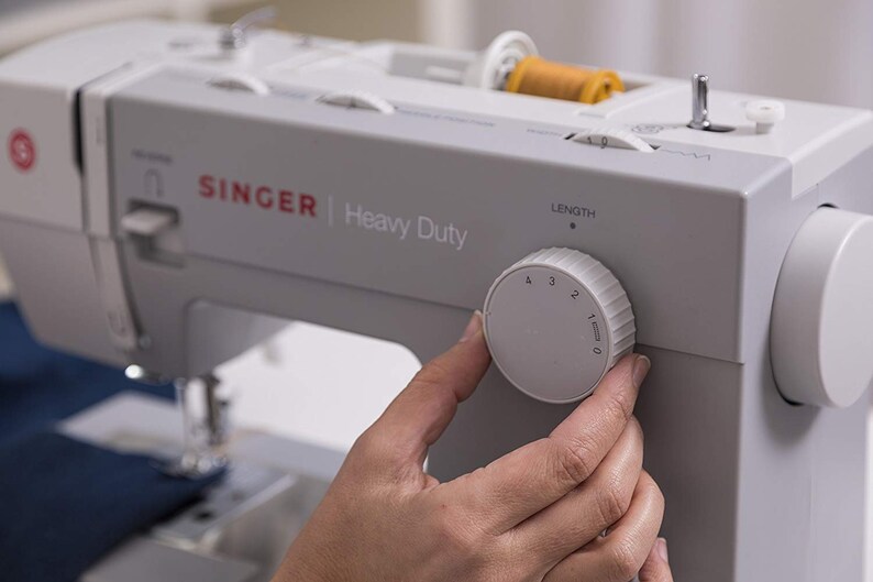May include: A white Singer Heavy Duty sewing machine with a knob to adjust the stitch length. The knob is labeled with numbers 0 through 4.