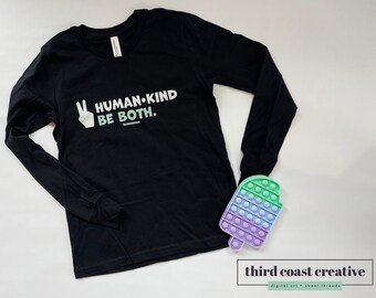 May include: Black long-sleeve shirt with a white peace sign and the text "HUMAN-KIND BE BOTH."  The shirt is laying on a white surface with a multi-colored pop-it toy.