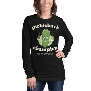 May include: Black long-sleeved shirt featuring a green cartoon pickle holding a shot glass of liquor and a pickleback. The text "pickleback champion of the world" is printed on the shirt.