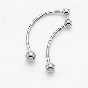 May include: Two silver-colored, curved barbell earrings. Each earring has a smooth, spherical ball at each end. The curved bar connects the two balls. The earrings are displayed against a white background.