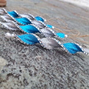 May include: A set of six blue and silver ribbon ornaments with white pearl accents. The ornaments are twisted and have a sparkly finish.