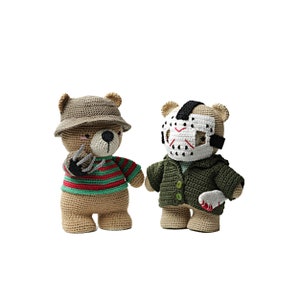 Puede incluir: Dos osos de peluche tejidos a crochet vestidos como personajes de películas de terror. Un oso lleva un sombrero marrón y una camisa a rayas rojas y verdes, sosteniendo una garra. El otro oso lleva una chaqueta verde y una máscara de hockey blanca.
