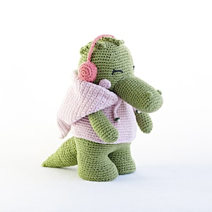 May include: A green crocheted alligator wearing a pink crocheted hoodie with a pink crocheted headband.