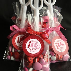 May include: Three clear plastic bags filled with red and pink candy, tied with red and white polka dot ribbon. Each bag has a white plastic shovel attached and a round red and white sticker that says "Valentine i DIG you! Happy Valentine's Day."