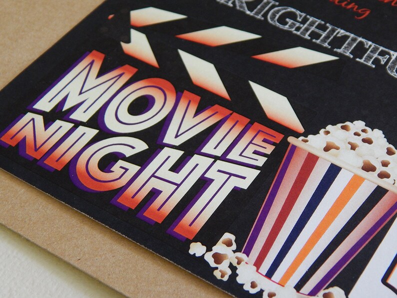 May include: A black card with the words "MOVIE NIGHT" in white, orange, and purple lettering. A popcorn bucket with red, white, blue, and orange stripes is on the right. A film clapperboard is at the top.