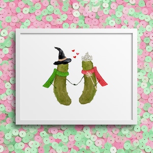 May include: A framed watercolor print featuring two anthropomorphic pickles holding hands. One pickle wears a witch hat and green scarf, the other a crown and red scarf. Small red hearts float above them. The background is a pink and green sequin pattern.