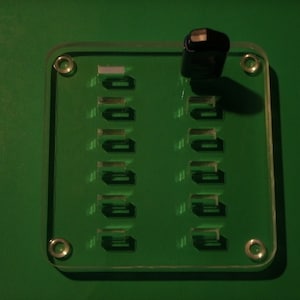 May include: A clear plastic panel with a grid of 10 rectangular openings. A black USB stick is placed on top of the panel.