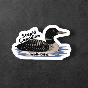 May include: A sticker featuring a cartoon illustration of a loon bird floating on water. The bird has a black head, white and black speckled body, and a red eye. Text on the sticker reads "Stupid Canadian" and "wolf bird".