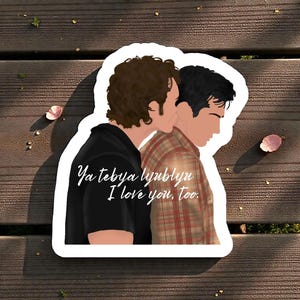 May include: A sticker with an illustration of two people in an embrace. One wears a black shirt, the other a red and brown plaid shirt. The text "Ya tebya lyublyu I love you, too." is written on the sticker.