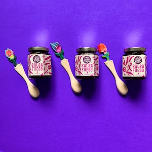 May include: Three small glass jars of salsa with colorful wooden spoons. Each jar has a label that says "Salsa Fuego" with a red chili pepper design.