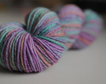 May include: A close-up of a skein of yarn with a mix of purple, pink, and green colors.