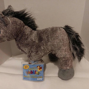 May include: A plush horse toy in shades of gray with a black mane and tail. The toy has a tag attached with the Webkinz logo. The horse is standing on a white surface.