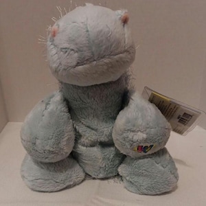 May include: A light blue plush hippo toy with pink accents on the ears. The stuffed animal has a soft, fuzzy texture and a tag attached. The toy is designed with large, rounded features.