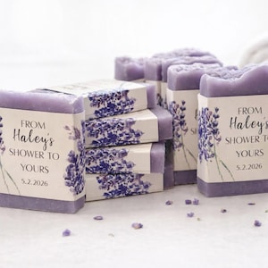 Peut inclure: Plusieurs savons de couleur lavande sont présentés sur une surface blanche. Chaque savon est emballé avec une étiquette florale et le texte "From Haley's Shower to Yours 5.2.2026". Des brins de lavande et une serviette blanche roulée sont en arrière-plan.