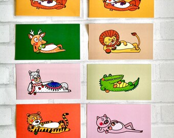 May include: Set of eight illustrated greeting cards featuring various animals, each holding a piece of fruit. The cards are printed on white cardstock with a colorful background. The animals include a fox, a deer, a lion, a llama, a crocodile, a tiger, and a pig.