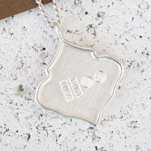 Peut inclure: Un collier pendentif en argent avec une forme ornée unique. Le pendentif a une surface texturée et est attaché à une chaîne délicate. Le pendentif a un motif sur la surface.