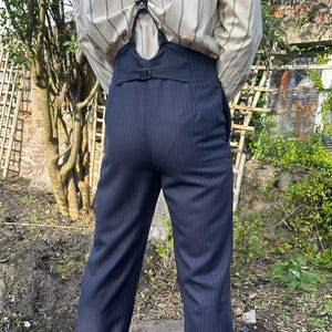 Puede incluir: Pantalones de raya diplomática azul marino con cintura alta y enganches para tirantes. Los pantalones se combinan con una camisa abotonada a rayas y tirantes azul marino. Adecuado para atuendos formales o de inspiración vintage.