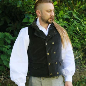 May include: A dark grey double-breasted waistcoat with gold buttons, worn with a white collared shirt and grey tweed trousers. The waistcoat has a velvet-like texture and a notched lapel. The outfit is suitable for historical reenactment or cosplay.