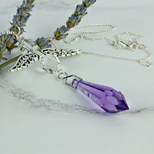 May include: A silver angel wing charm necklace with a clear crystal and a purple crystal pendant.