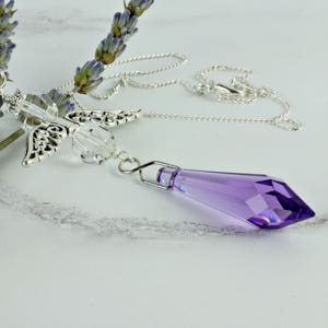 May include: A silver chain necklace with a crystal pendant and a silver angel wing charm. The pendant is a purple crystal with a faceted design.