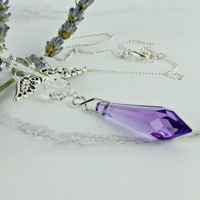 May include: A silver chain necklace with a crystal pendant and a silver angel wing charm. The pendant is a purple crystal with a faceted design.