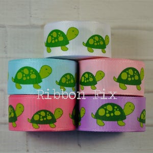 May include: Five spools of ribbon with a green turtle pattern. The ribbons are in the colors white, light blue, pink, and lavender.