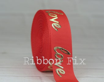 May include: A roll of red grosgrain ribbon with the word "love" printed in gold. The ribbon is tightly wound, showing the texture of the fabric. The gold lettering is slightly raised, adding dimension to the design.
