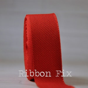 May include: A roll of bright red woven ribbon. The ribbon is textured and has a slight sheen. The text "Ribbon Fix" is visible in the lower left corner of the image.