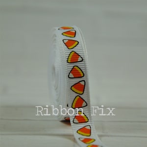 May include: Rolled white ribbon featuring a repeating pattern of candy corn in orange, yellow, and black. The text "Ribbon Fix" is printed on the ribbon's surface.