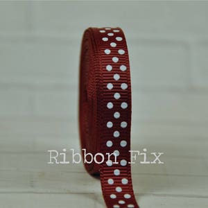 May include: A roll of burgundy ribbon with white polka dots. The ribbon is tightly wound, displaying a textured surface. The text "Ribbon Fix" is printed on the ribbon. This ribbon is suitable for crafts, gift wrapping, and decorative projects.