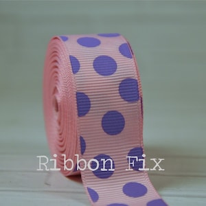 May include: A roll of pink grosgrain ribbon featuring large purple polka dots. The ribbon has a ribbed texture and the text "Ribbon Fix" is visible on the ribbon.