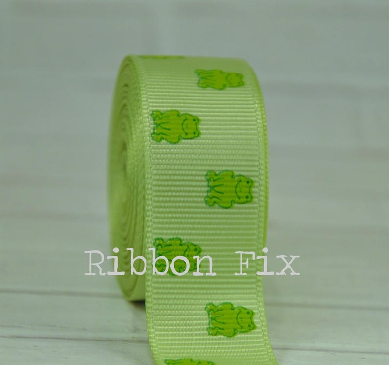May include: Green ribbon with a repeating pattern of green frogs. The ribbon is rolled up and the text "Ribbon Fix" is visible in the lower center of the image.