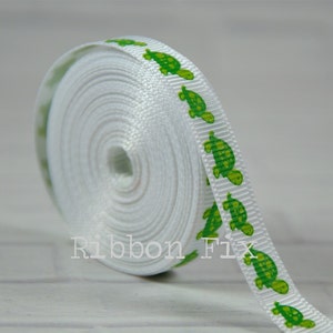 May include: A roll of white ribbon with a repeating pattern of green turtles. The ribbon is tightly wound, showing the texture of the material. The text "Ribbon Fix" is visible on the ribbon.