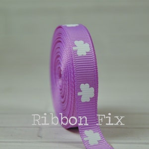 May include: A roll of purple ribbon with white four-leaf clover designs. The ribbon is 1 inch wide.