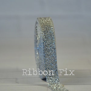 May include: A roll of silver glitter ribbon. The ribbon is rolled up and the end is hanging down. The ribbon is shiny and sparkly.