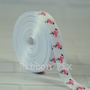 May include: White satin ribbon with pink flamingo print. The ribbon is rolled up and the end of the ribbon is visible. The ribbon is labeled "Ribbon Fix".