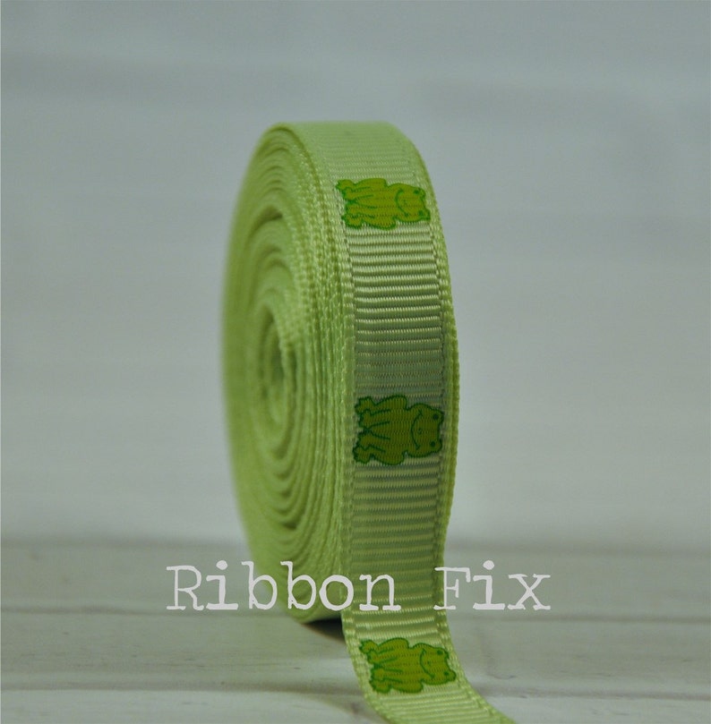 May include: A roll of light green ribbon with a repeating pattern of green frogs. The ribbon is 1 inch wide and is perfect for adding a touch of whimsy to crafts, gifts, and home decor.
