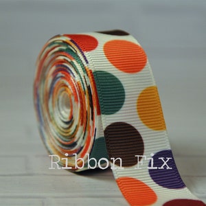 May include: A roll of white ribbon with colorful polka dots in orange, brown, green, purple, and yellow. The ribbon is 1.5 inches wide.