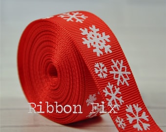 Könnte beinhalten: Rotes Band mit weißen Schneeflocken-Designs. Das Band ist aufgerollt und das Schneeflockenmuster ist auf der Außenseite der Rolle sichtbar.