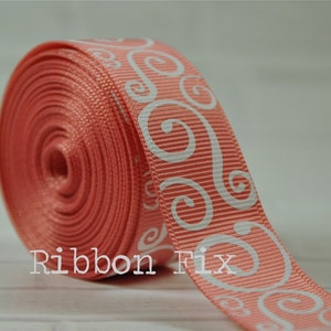 May include: A roll of coral pink ribbon with a white swirl pattern. The ribbon is 1.5 inches wide.