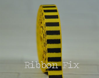 May include: A spool of yellow ribbon with evenly spaced black stripes. The ribbon is tightly wound, displaying a repeating pattern. The text "Ribbon Fix" is visible on the ribbon. This ribbon is suitable for crafting and decorative purposes.