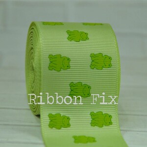 May include: Green ribbon with a repeating pattern of green frogs. The ribbon is on a white surface. The text "Ribbon Fix" is visible in the image.