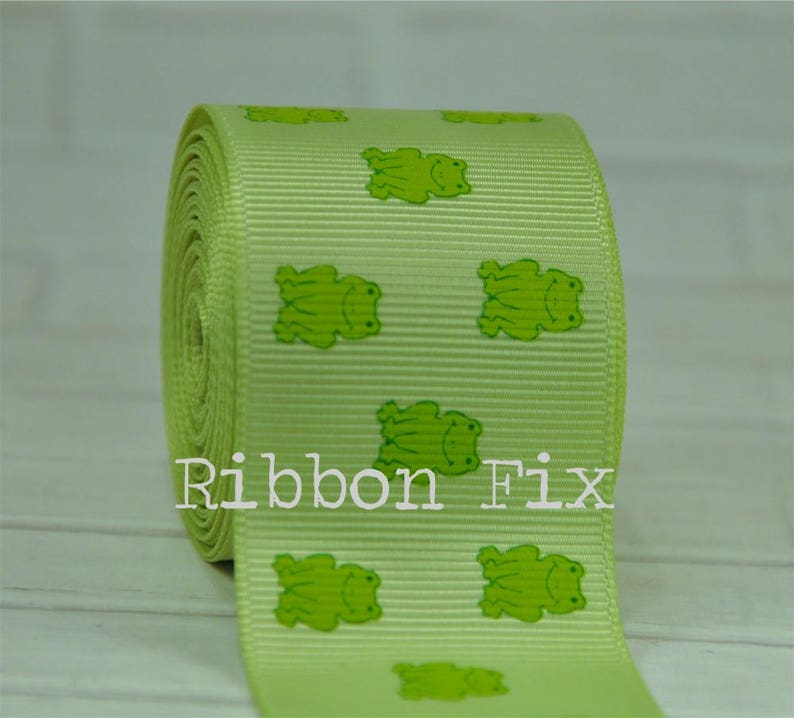 May include: Green ribbon with a repeating pattern of green frogs. The ribbon is on a white surface. The text "Ribbon Fix" is visible in the image.