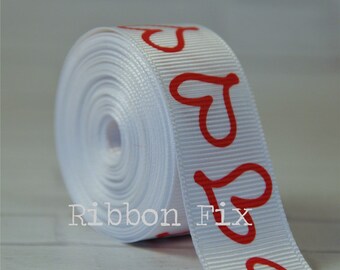 May include: White satin ribbon with red heart designs. The ribbon is rolled up and the hearts are visible on the outside of the roll.