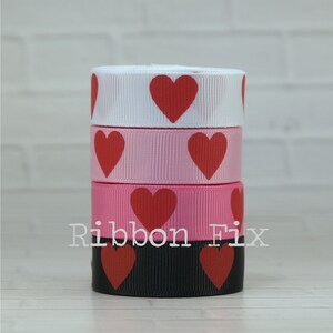 May include: Four spools of ribbon with red hearts printed on them. The ribbons are white, pink, pink, and black.