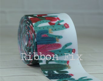 May include: A roll of white ribbon featuring a repeating pattern of green cacti with pink flowers. The text "Ribbon Fix" is printed on the ribbon. The ribbon is likely used for crafting or decorative purposes.