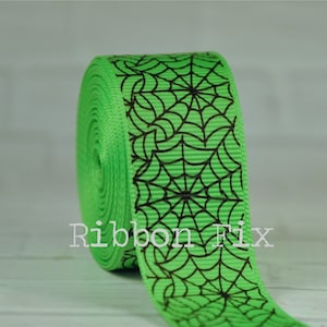 May include: Green ribbon with a black spiderweb pattern.  The ribbon is rolled up and the pattern is visible on the front and side of the roll.
